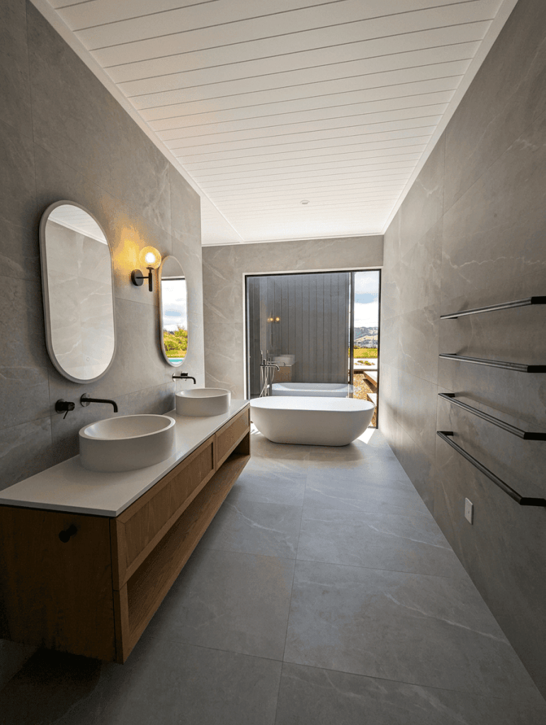 Luxurious high end tiled bathroom with large picture window and bath with a view Matakana